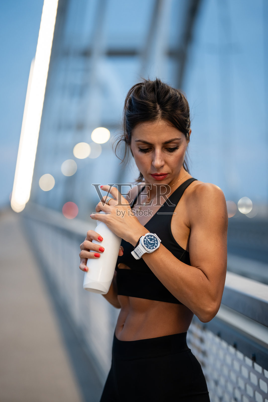 运动女性在桥上训练后手持水瓶照片摄影图片