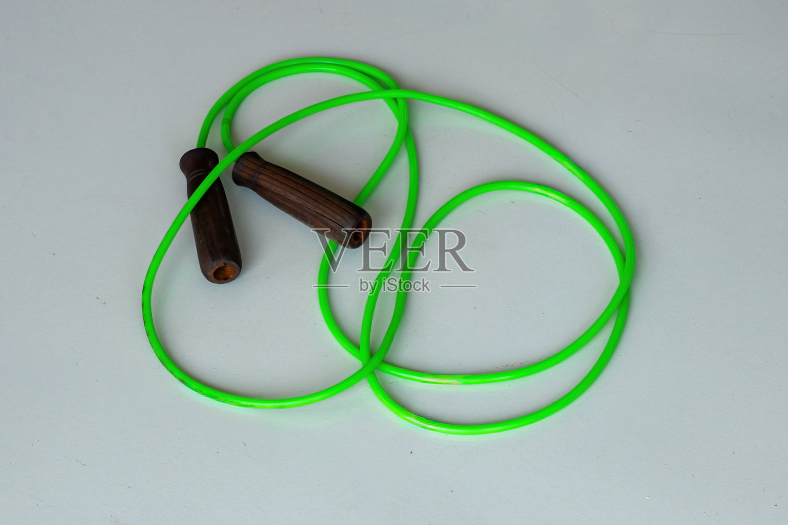 特写镜头展示一根绿色的跳绳，木制手柄，静静地躺在白色瓷砖的健身房地板上，随时准备开始锻炼。非常适合健身、运动和体育主题。照片摄影图片