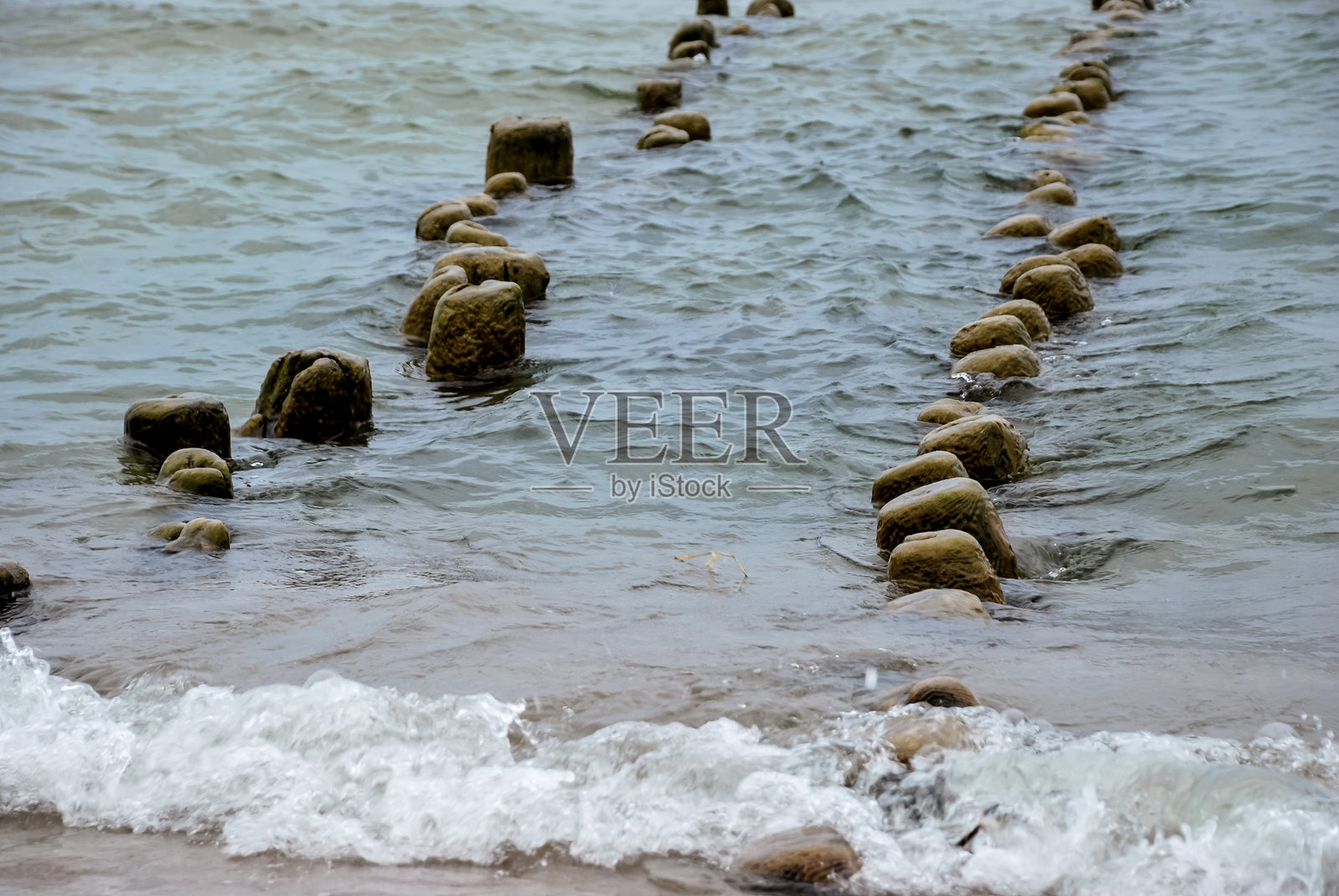风化的岩石在平静的蓝色海洋中，沿着沙滩延展照片摄影图片