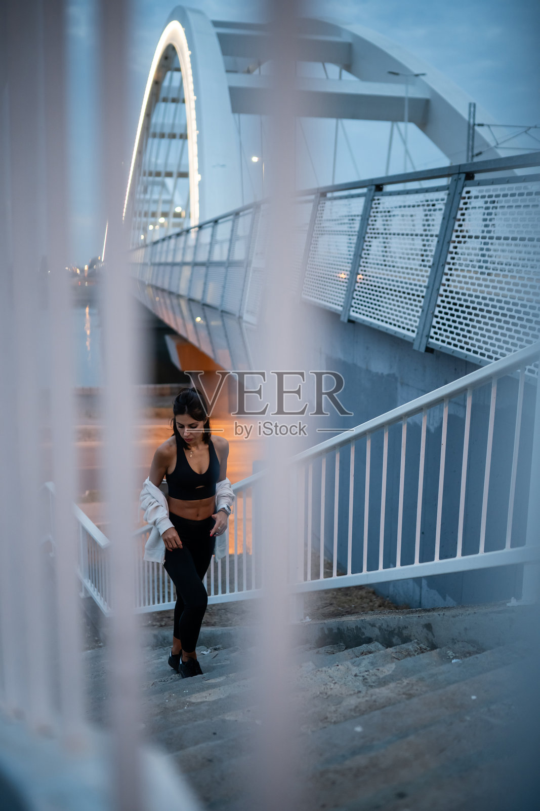 年轻的女运动员在训练后走下现代桥旁的楼梯照片摄影图片