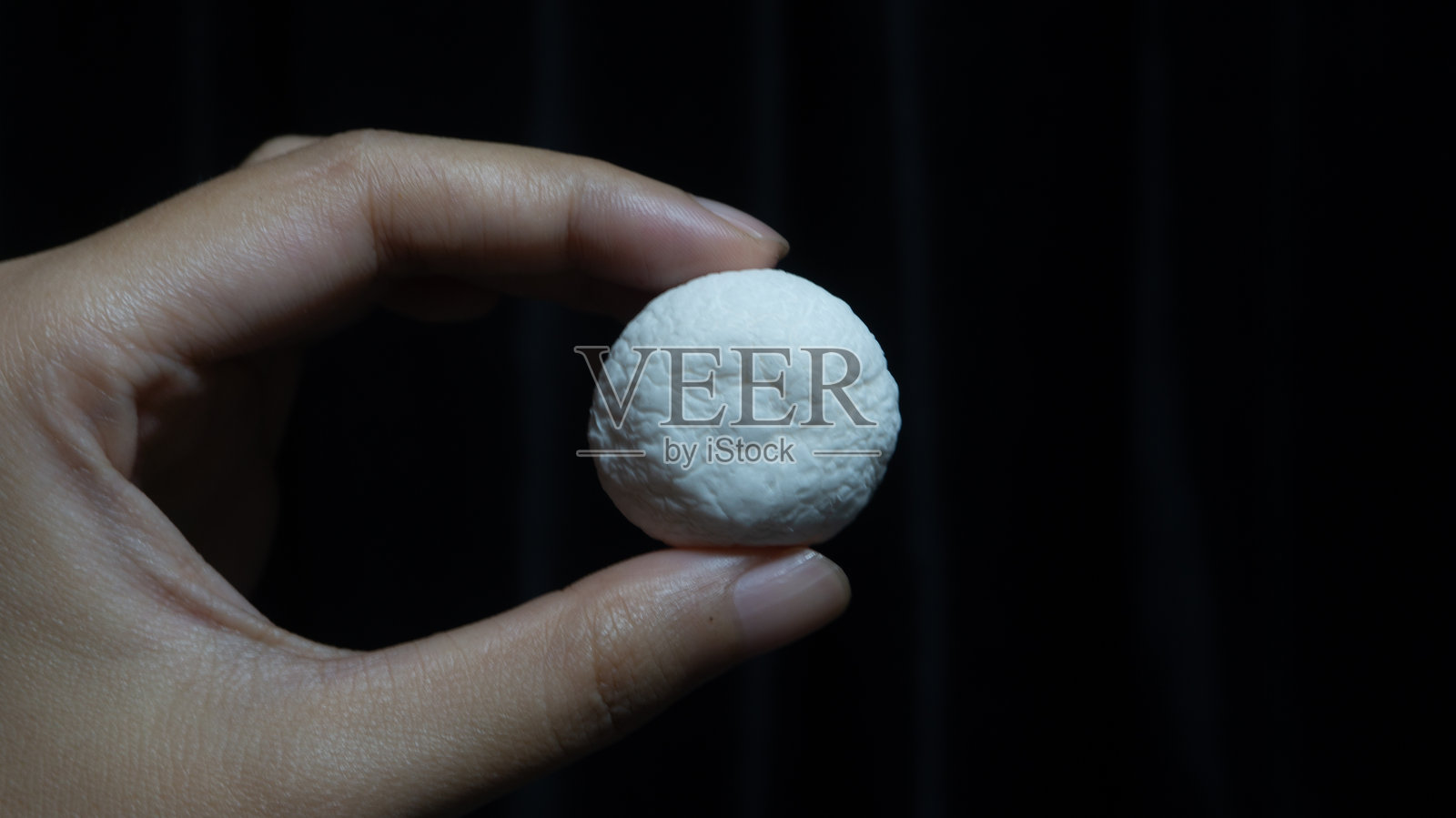 手轻柔地握着一个白色的、有纹理的球体，背景中性，形成对比。照片摄影图片