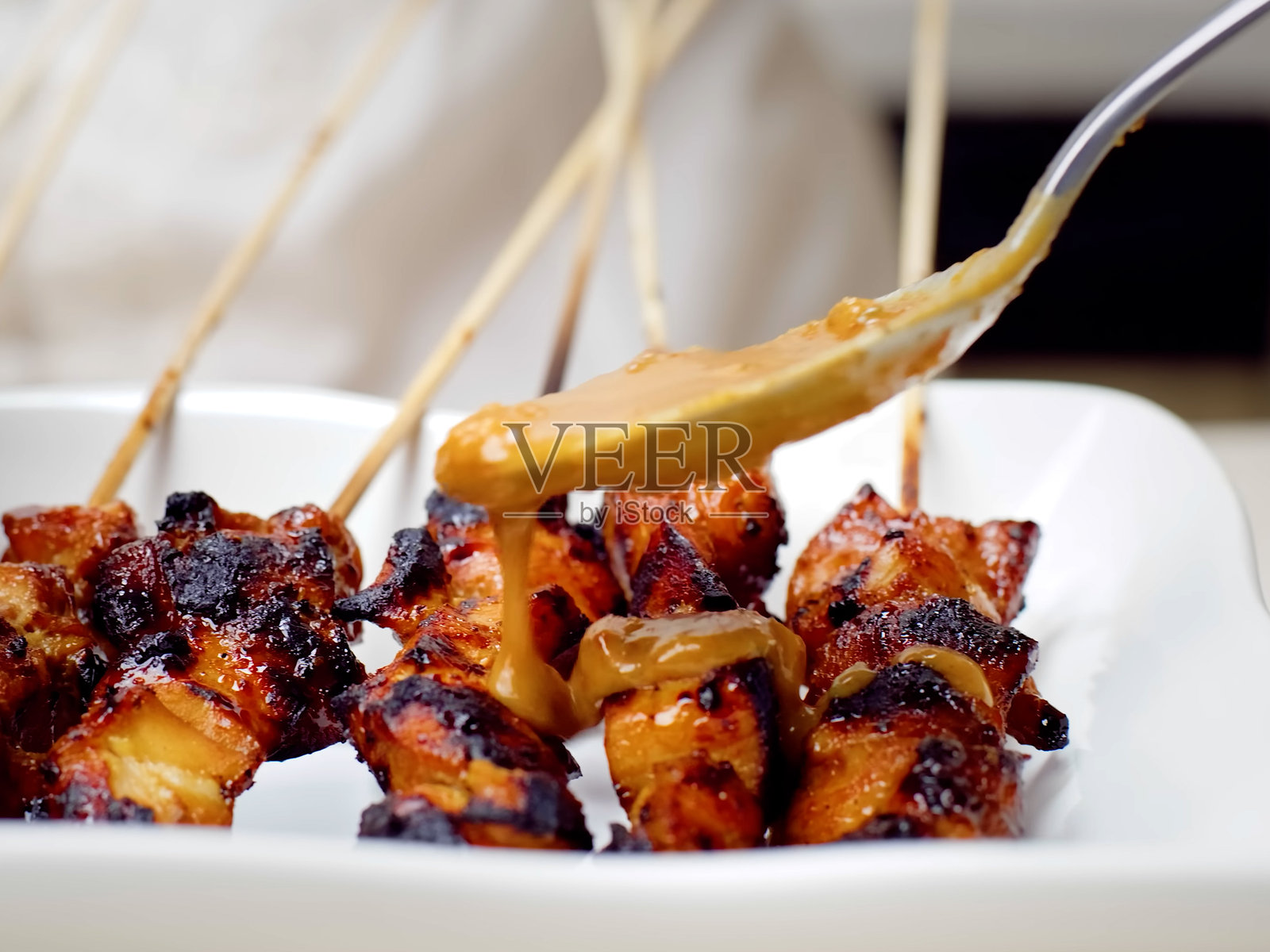 酱汁从勺子上倒在木签上的炸肉块上，餐厅的烤肉制作过程特写照片摄影图片