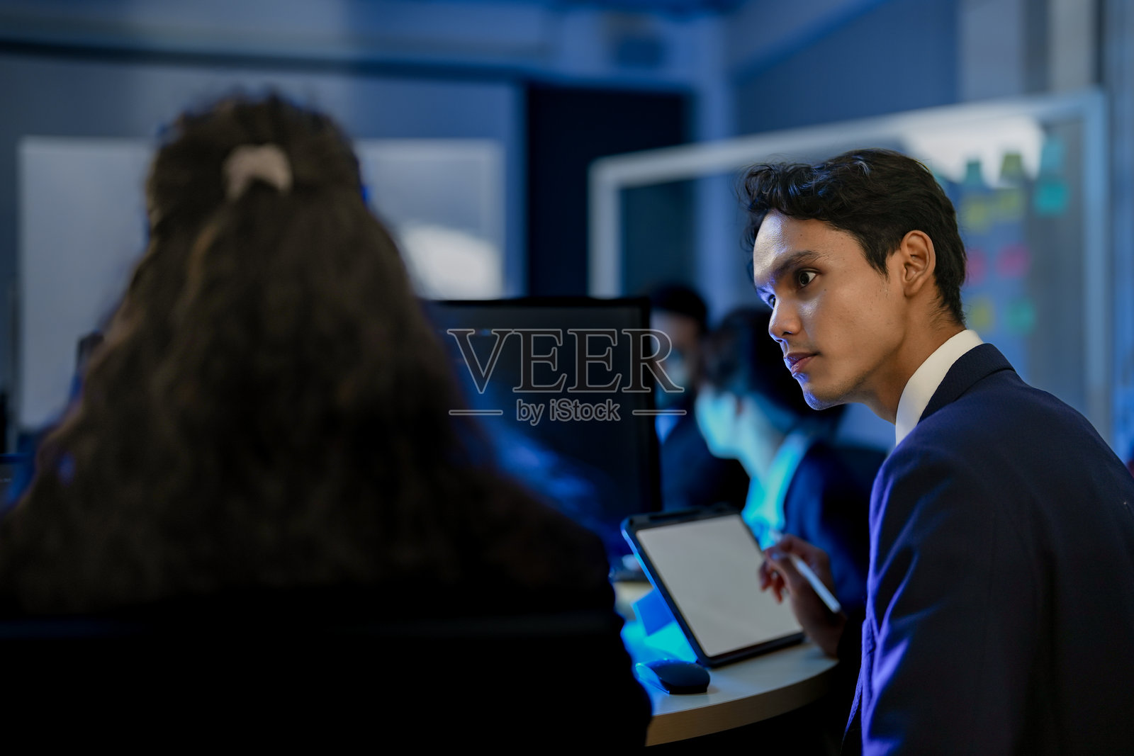 一位经理在夜晚的现代办公室里带领着他多元化的年轻专业团队。他指着电脑屏幕，解释项目并培训员工。照片摄影图片