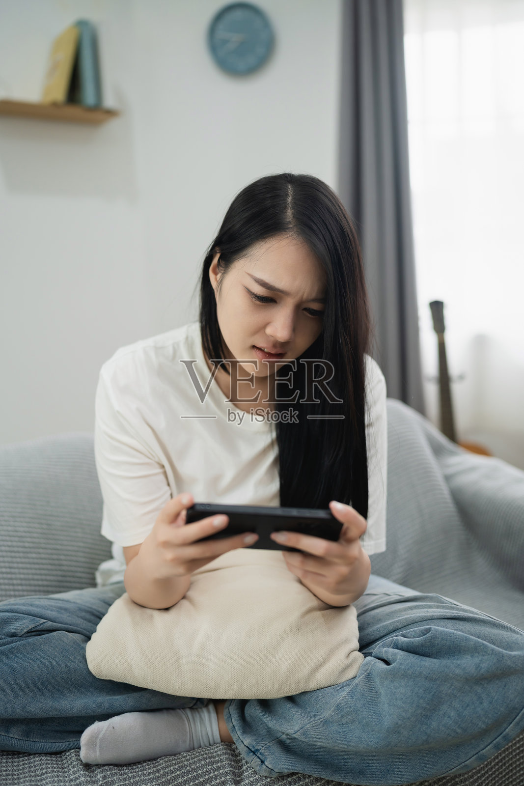 年轻女性坐在沙发上，穿着休闲服，感到沮丧，正在家中玩手机游戏，周围氛围温馨舒适。照片摄影图片