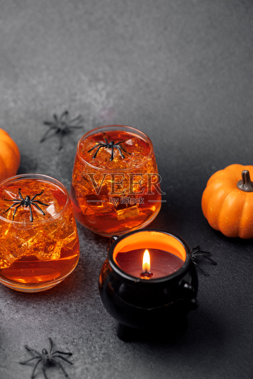 万圣节主题饮品，配有冰块、小南瓜和阴森的蜘蛛装饰，摆放在黑色表面上照片摄影图片