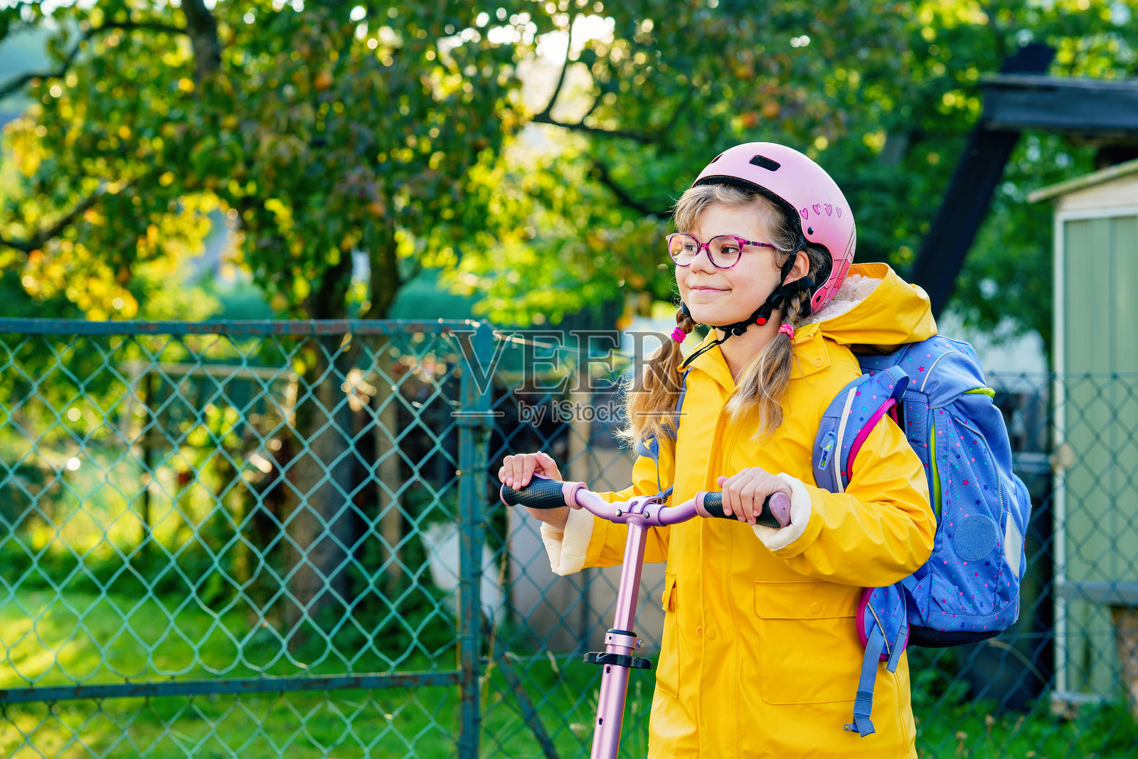 快乐的小学生骑着滑板车上学，戴着头盔和背包。安全、活跃，真实可爱的孩子在城市中通勤。照片摄影图片