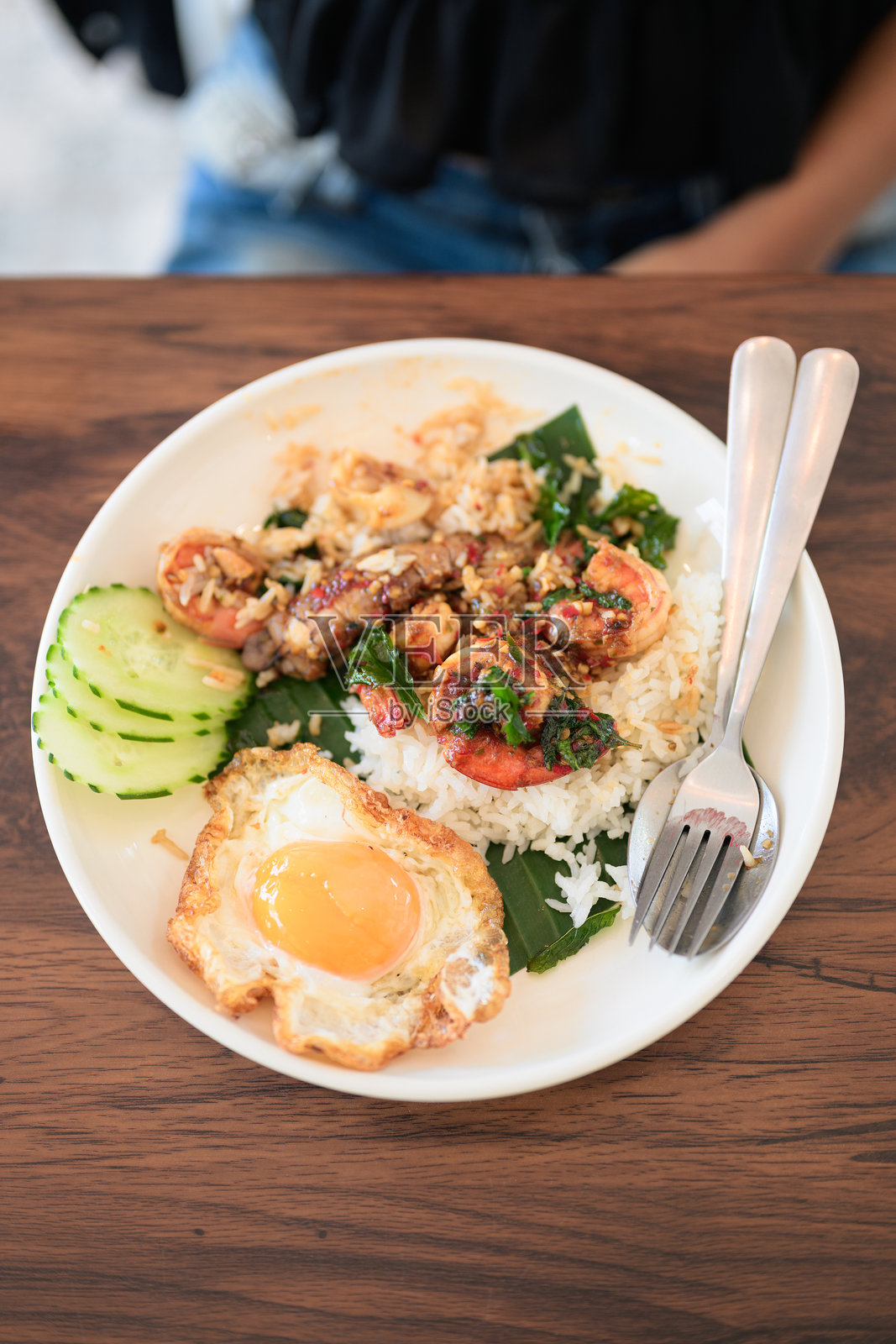 餐厅里，女人特写镜头正在享用泰式罗勒海鲜菜肴，配有煎蛋和米饭。照片摄影图片