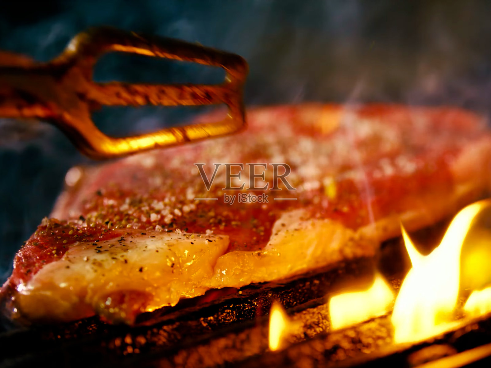 一块美丽多汁的肉在烤架上烤制，火焰和烟雾可见，特写，黑色背景。照片摄影图片