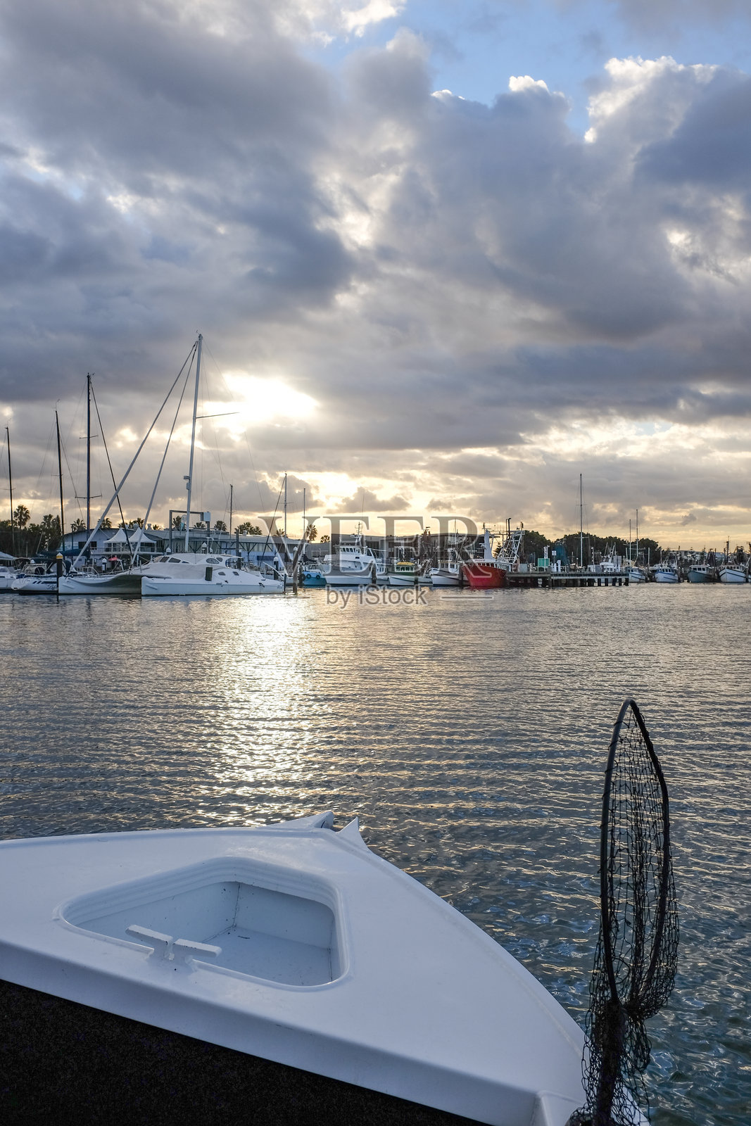 夕阳西下，照耀着停满船只的码头，温暖的倒影映在平静的水面上。照片摄影图片