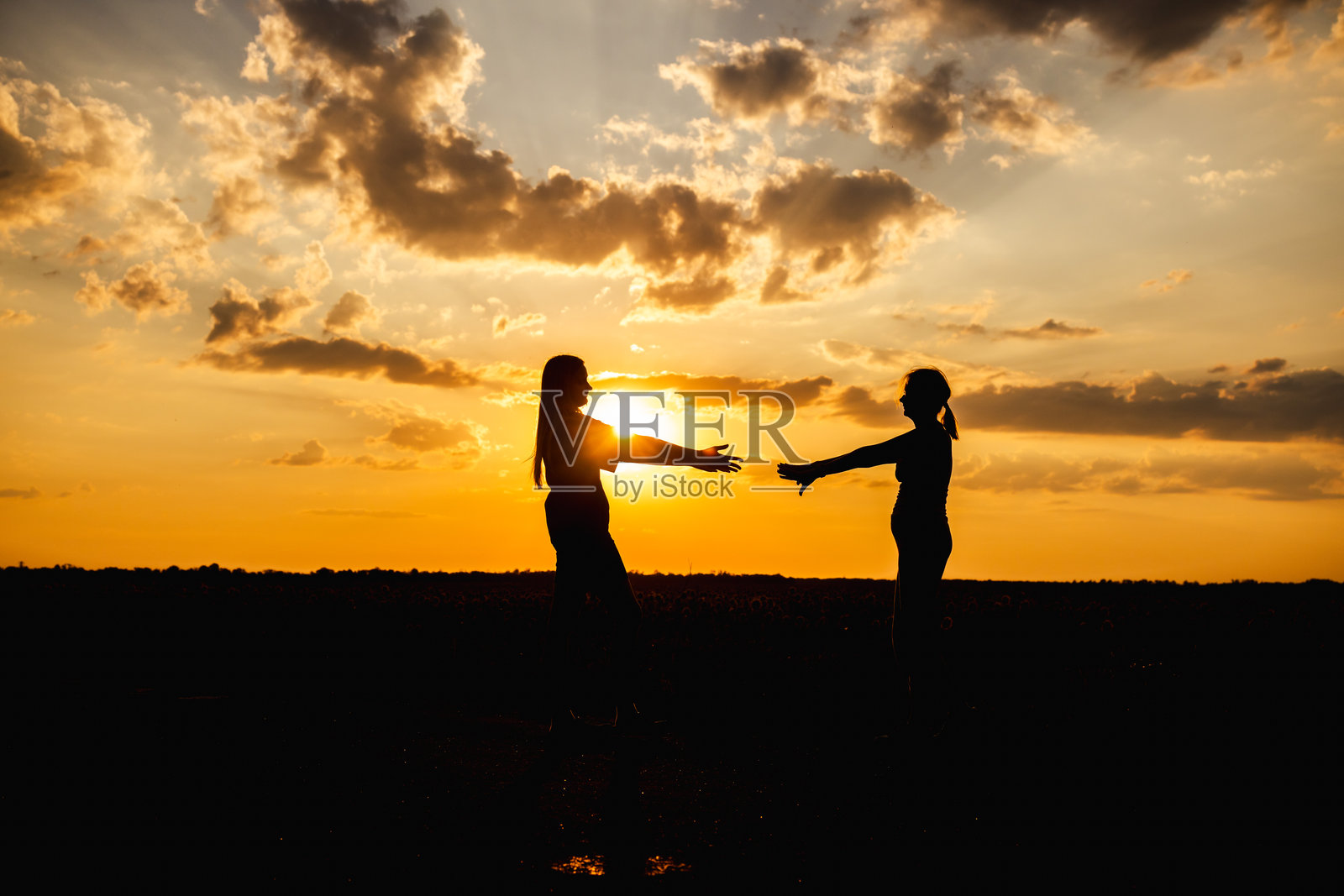 日落时分，两位女性的剪影伸出手来相拥照片摄影图片