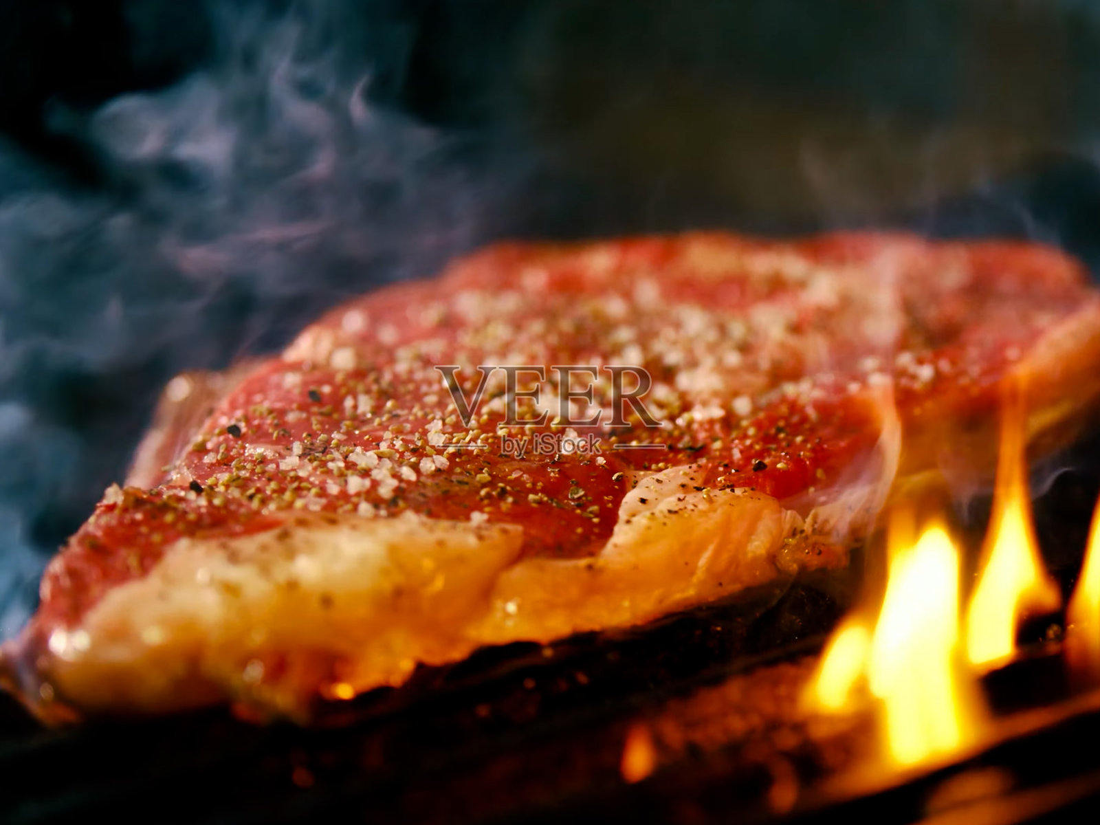 一块美丽多汁的肉在烤制，火焰和烟雾可见，特写，背景为黑色。照片摄影图片