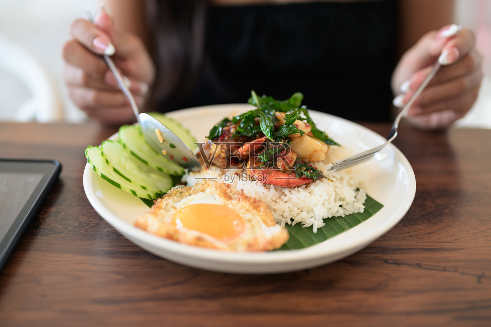 餐厅里，女人特写镜头正在享用泰式罗勒海鲜饭配煎蛋和米饭照片摄影图片