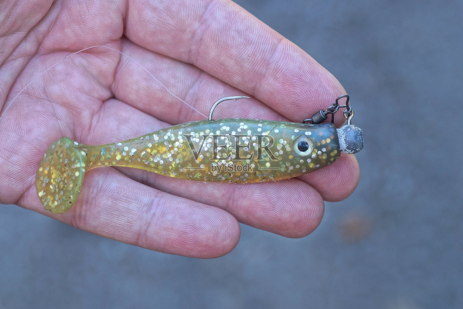 手握一只带钢钩的黄色硅胶鱼照片摄影图片