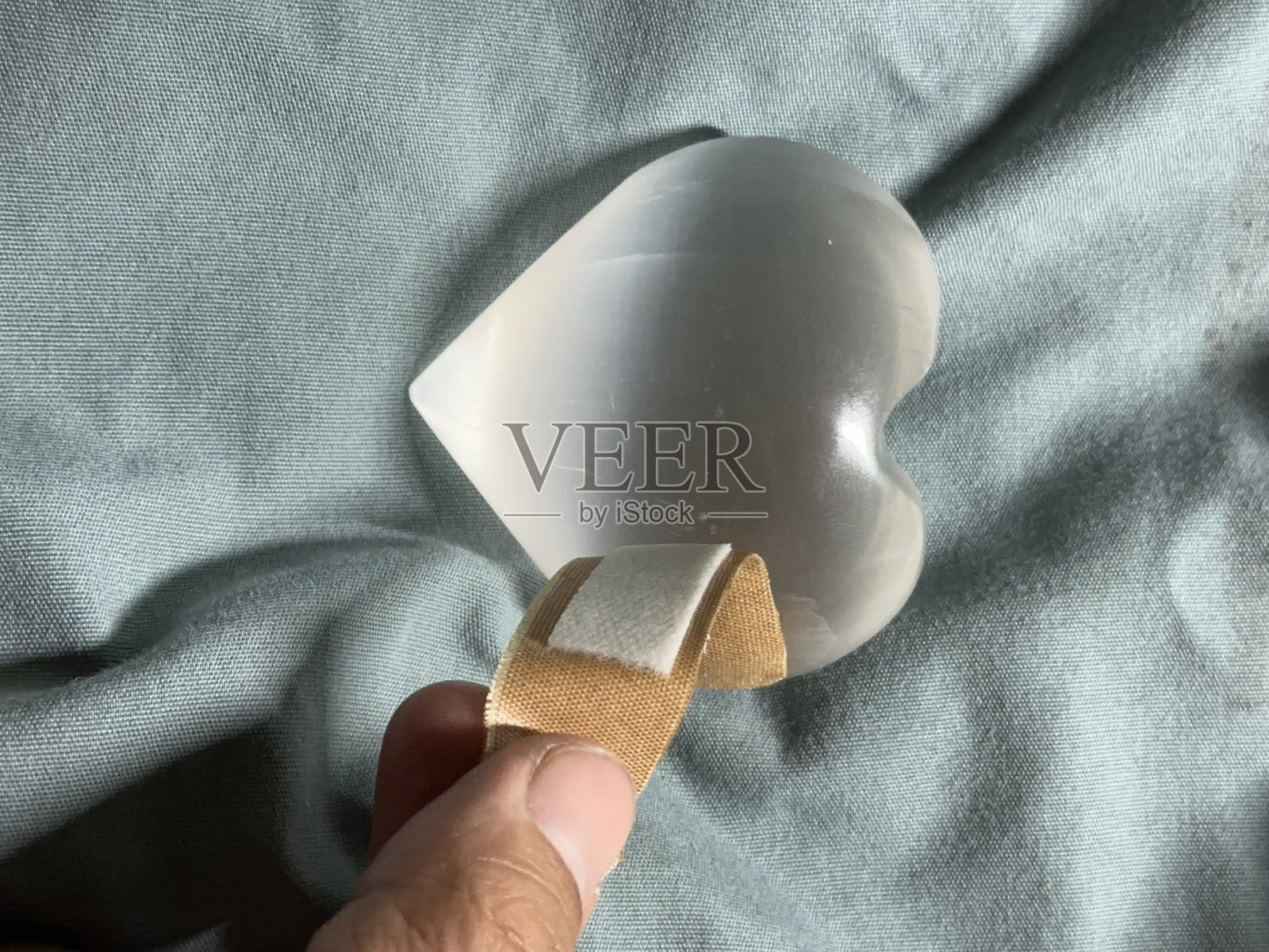 绿色手术服背景上剥落的心形水晶绷带，无面部照片摄影图片