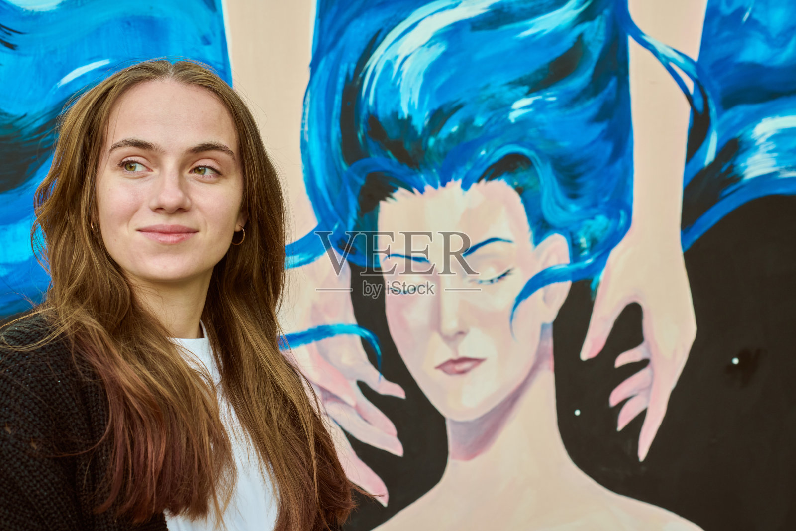 年轻女子在色彩斑斓的壁画旁微笑，拥有蓝色头发。照片摄影图片