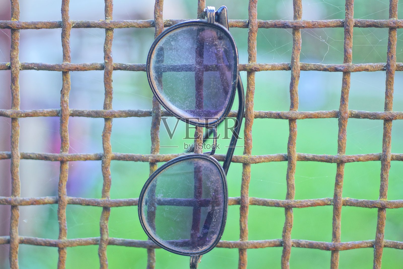 一副黑色塑料太阳镜挂在棕色生锈的铁格栅上照片摄影图片