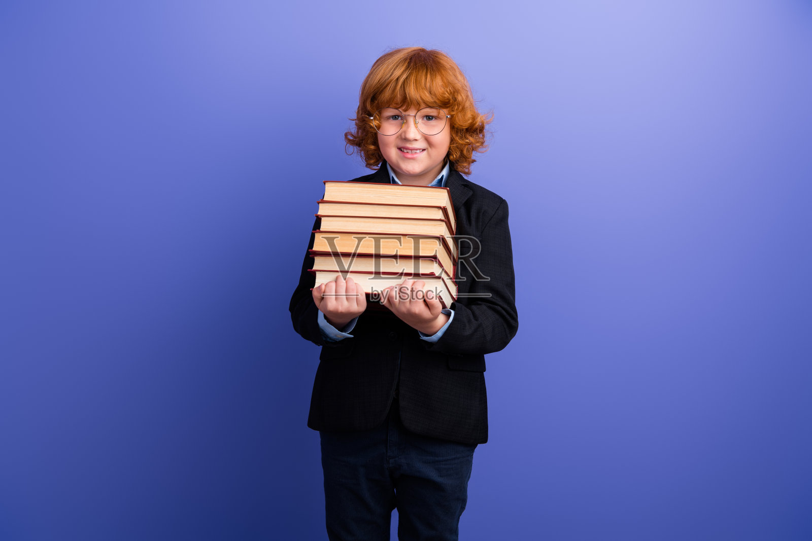 快乐聪明的学生露齿而笑，双手抱着一堆书，背景为紫色。照片摄影图片