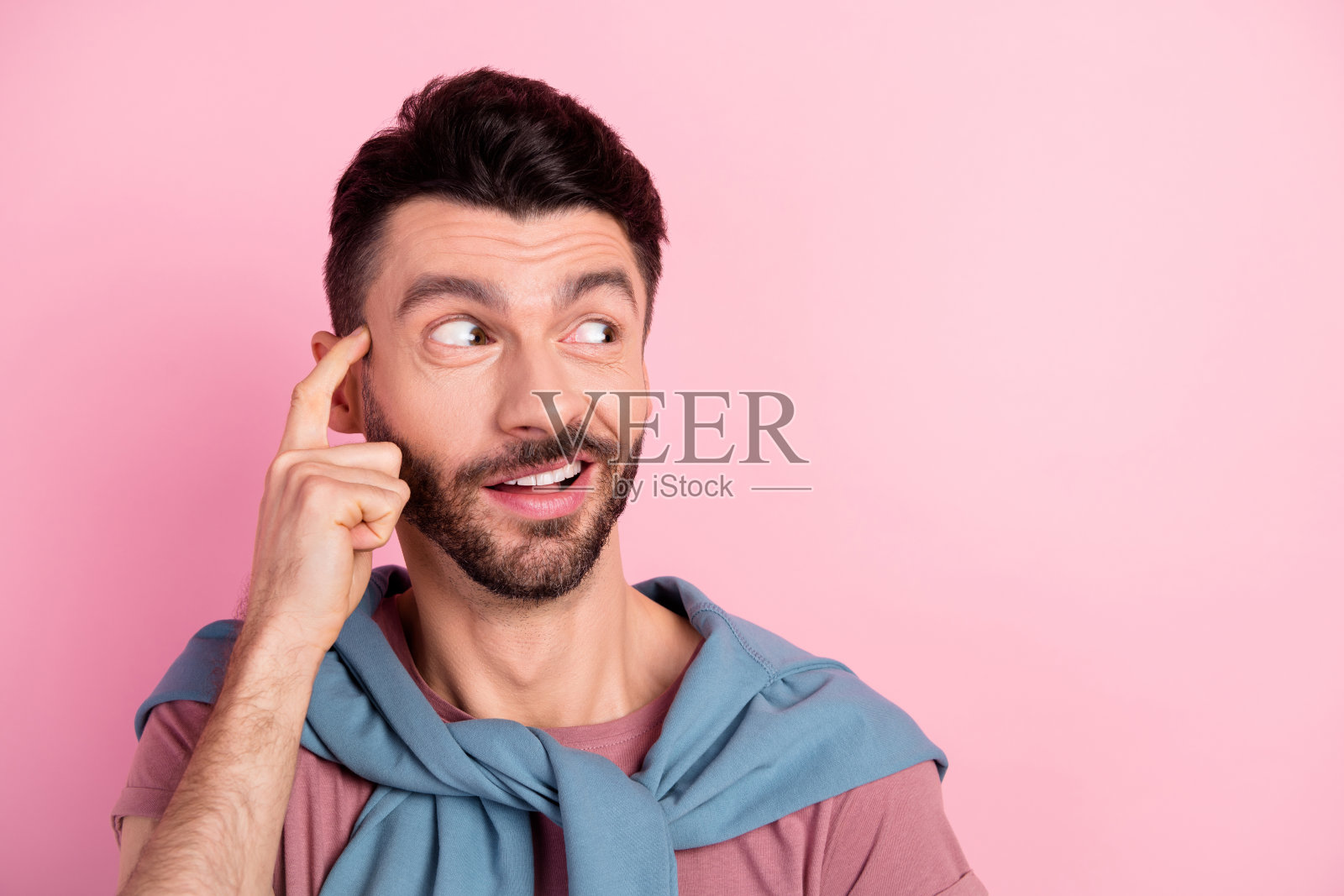 年轻男孩惊讶地看着空旷的空间，手指轻触太阳穴，背景为粉色。照片摄影图片