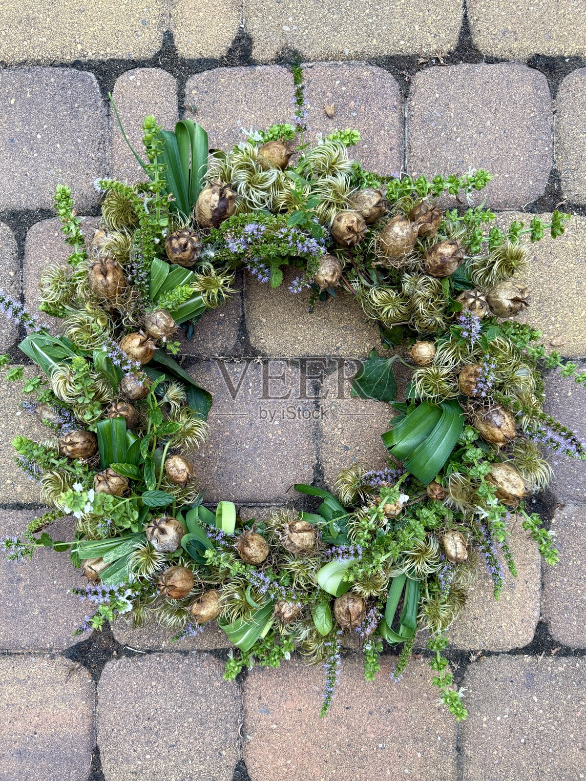 装饰性的鲜枝、花朵和叶子编成的花环，搭配紫色丝带，悬挂在靠近房子前门的浅色墙壁背景上。照片摄影图片