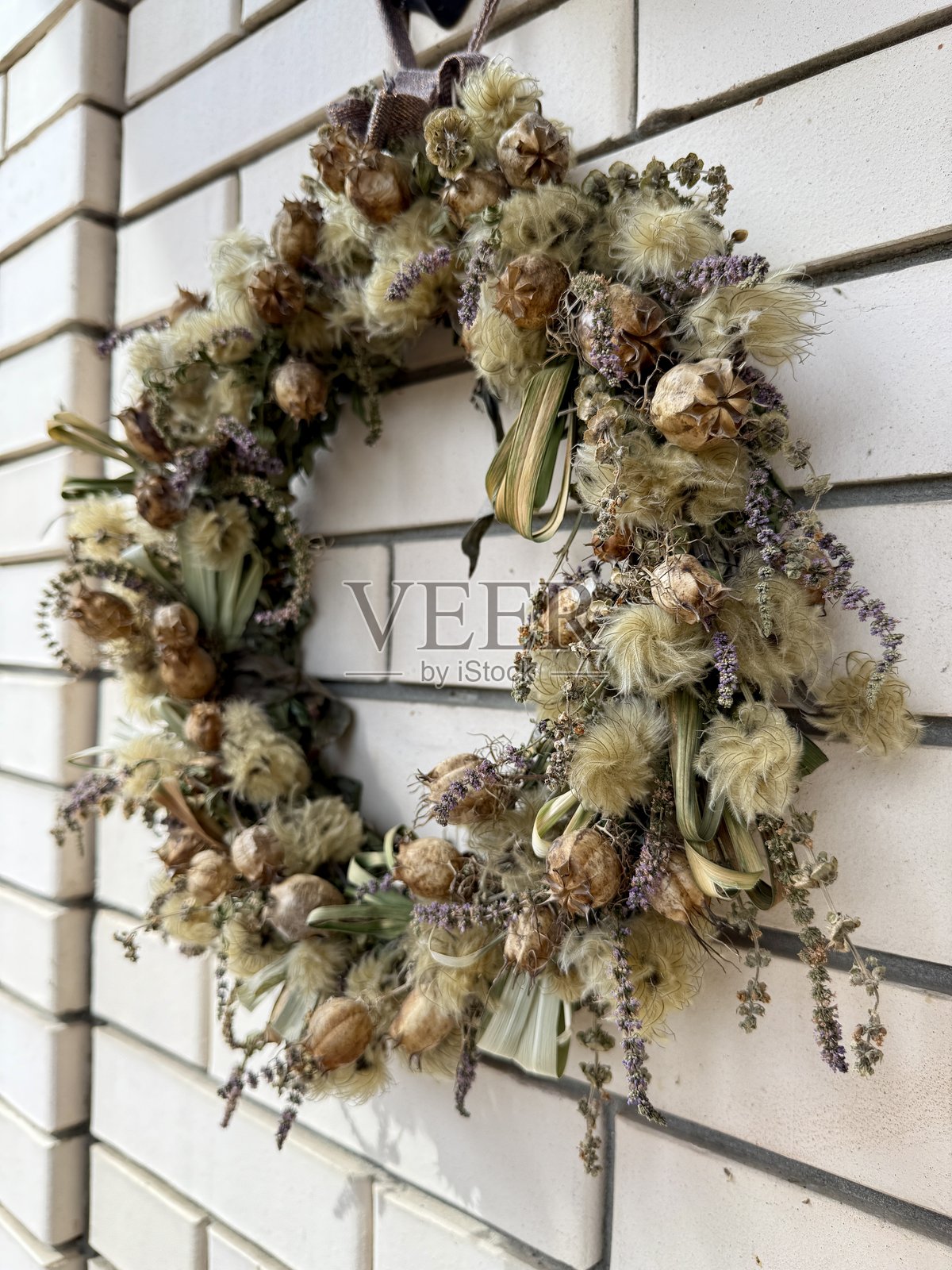 装饰性的鲜枝、花朵和叶子编成的花环，搭配紫色丝带，悬挂在靠近房子前门的浅色墙壁背景上。照片摄影图片