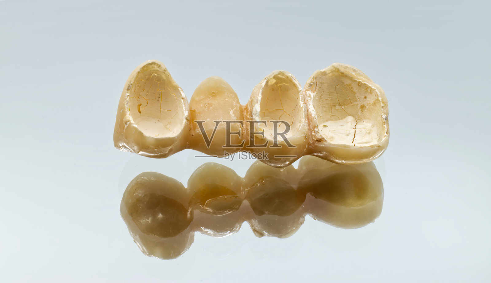 一个磨损或临时的牙桥，上面有多个牙冠，展示在一个反光的表面上。照片摄影图片