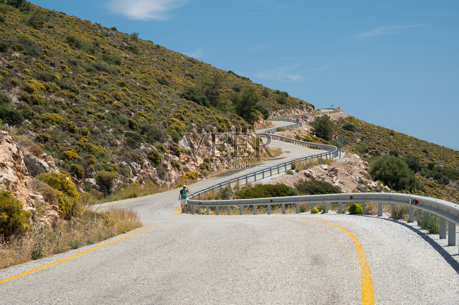 希腊蜿蜒的山路上，一名徒步旅行者正在向上攀登。照片摄影图片