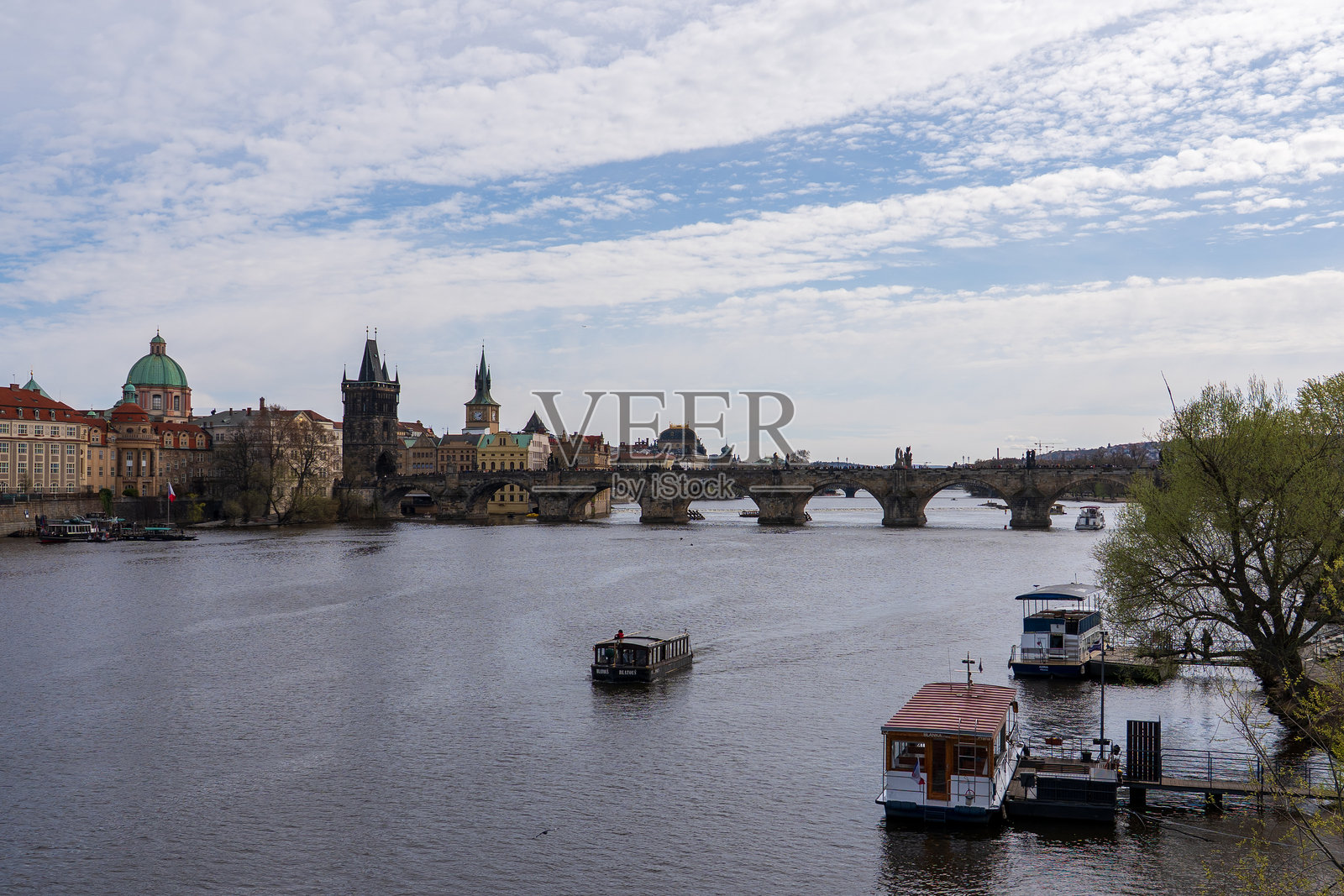 捷克共和国布拉格 - 2025年4月5日：查尔斯桥和伏尔塔瓦河的景观，船只经过。照片摄影图片