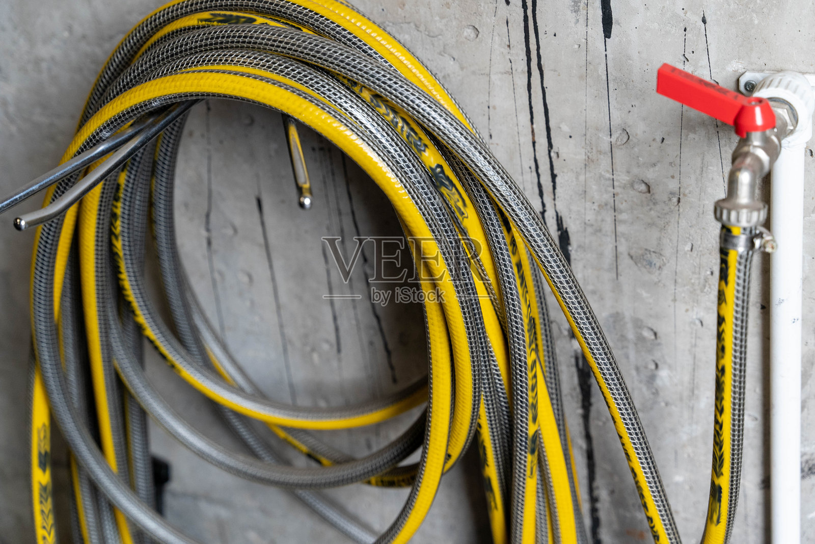 黄色花园水管挂在混凝土墙上，旁边有一个红色水龙头。照片摄影图片