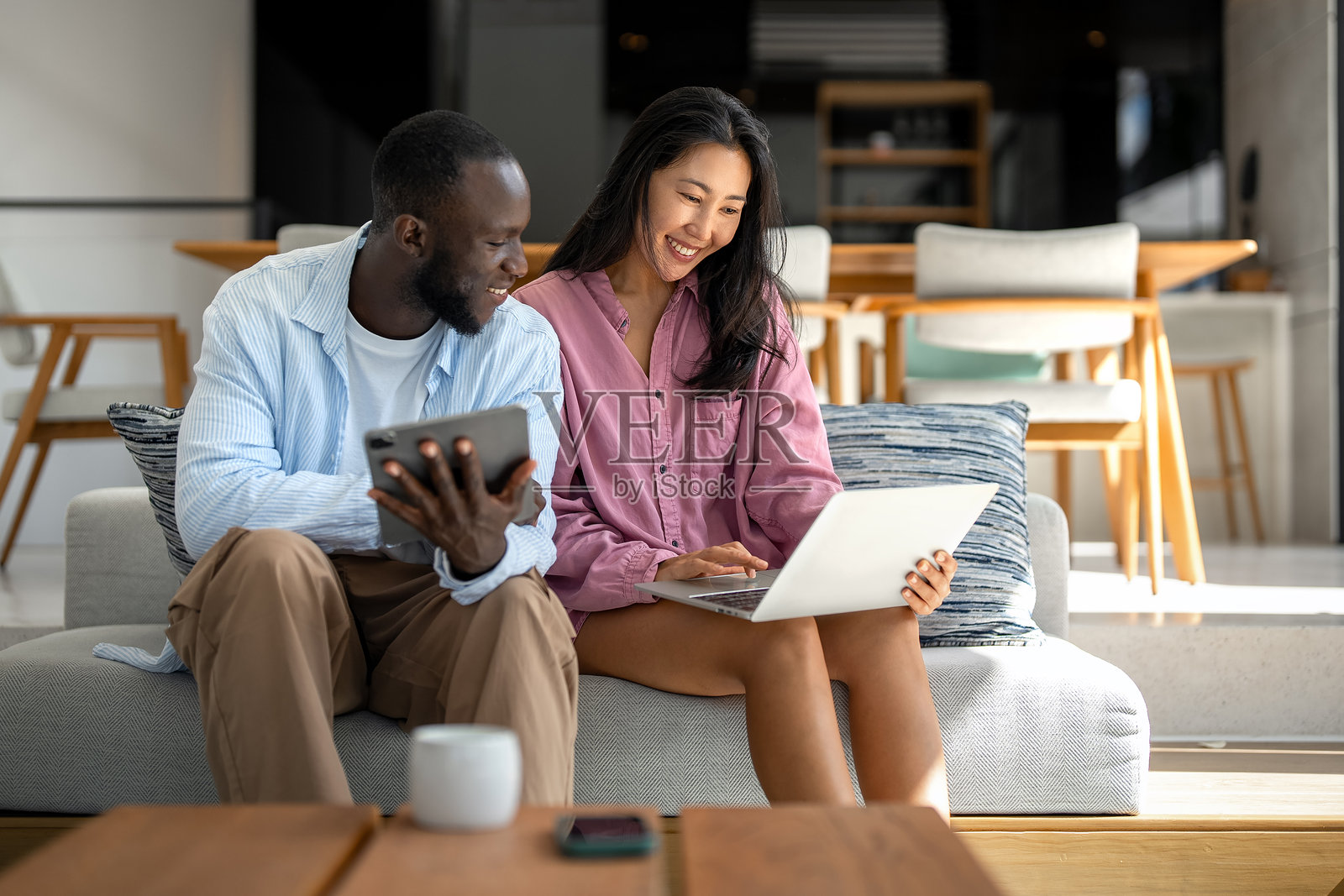 年轻快乐的多民族情侣在家中使用笔记本电脑和数字设备享受乐趣照片摄影图片