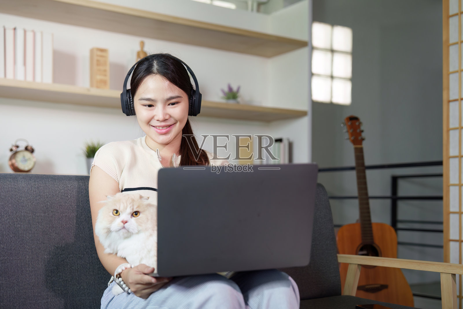 在家远程工作与猫咪相伴。年轻女性戴着耳机，正在笔记本电脑上工作。照片摄影图片