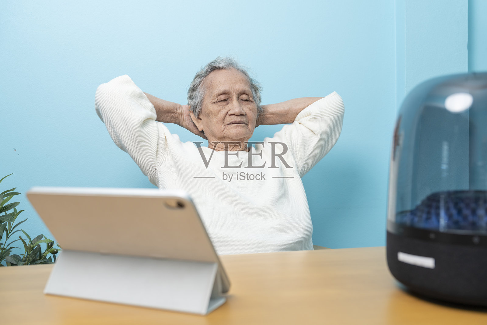 一位年长的亚洲女性正在通过无线音箱从数字平板电脑上听音乐。照片摄影图片