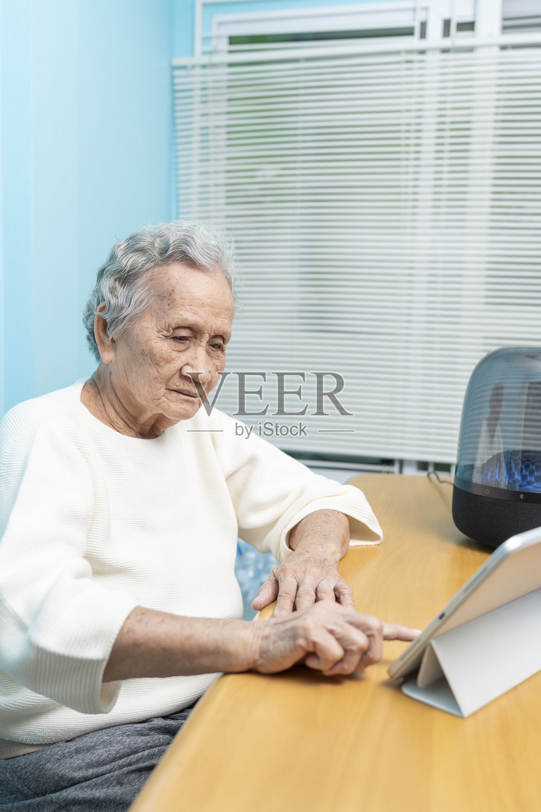 一位年长的亚洲女性正在使用数字平板电脑在线搜索音乐，并通过无线扬声器听音乐。照片摄影图片