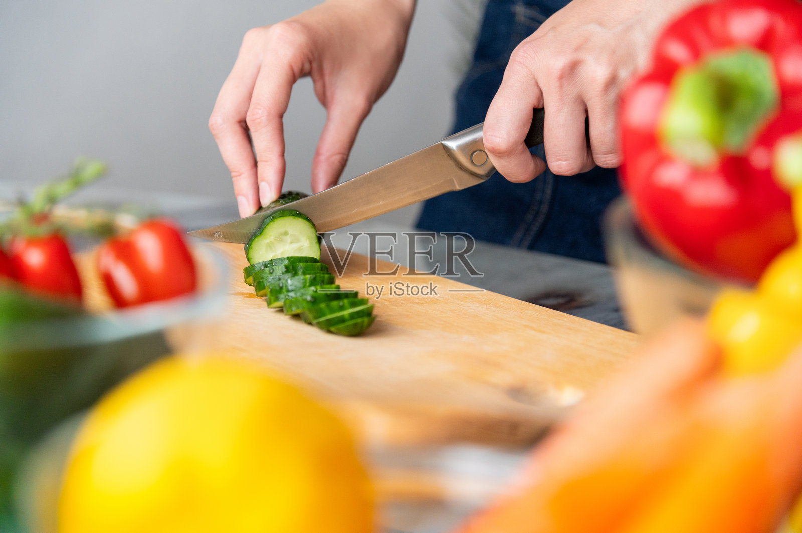 厨房里的手、切菜板和沙拉，搭配绿色蔬菜，适合健康饮食。一个有烹饪技巧的人在家准备午餐，使用沙拉、黄瓜和有机食材。照片摄影图片