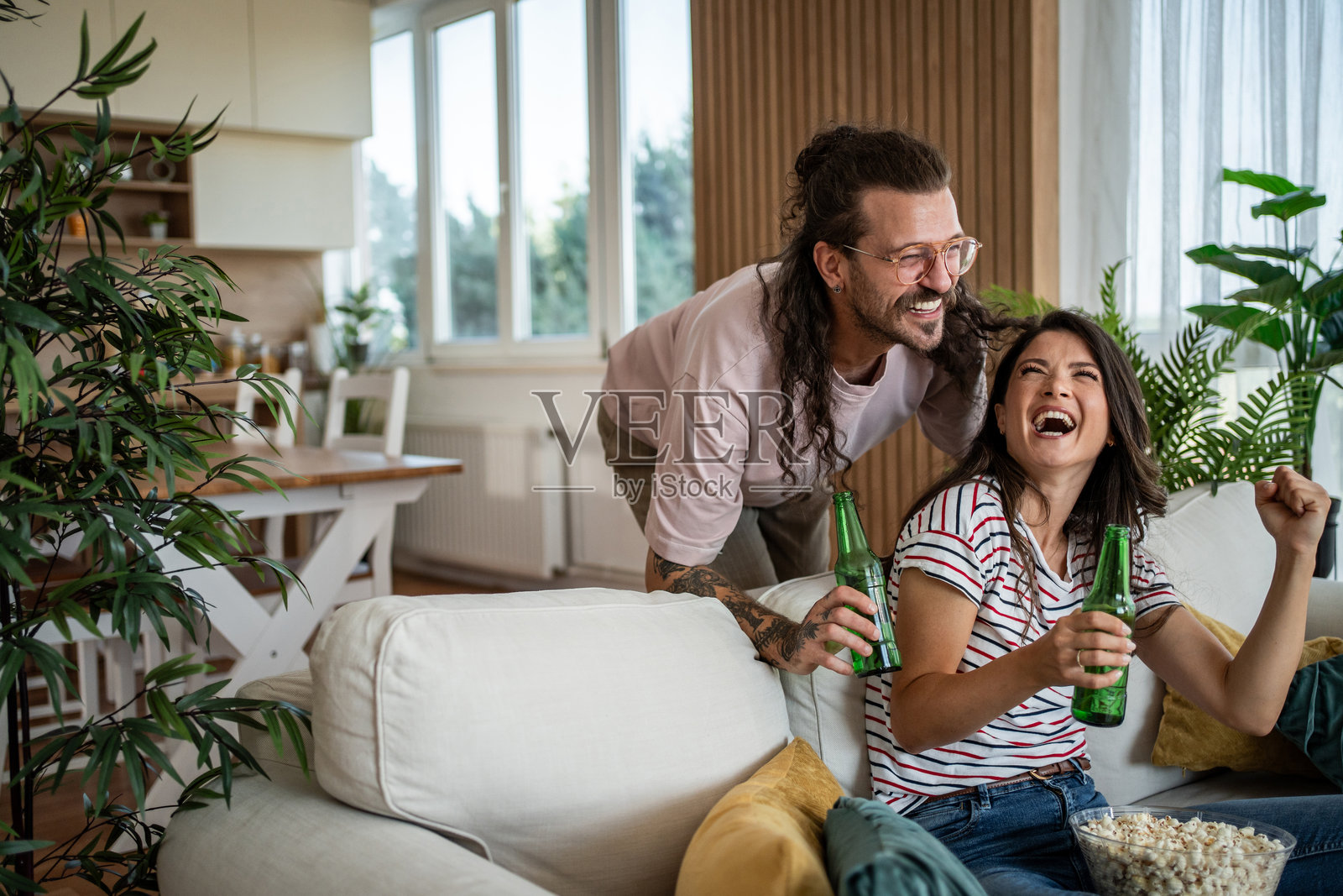年轻情侣在家看电视时欢笑并为体育比赛加油照片摄影图片
