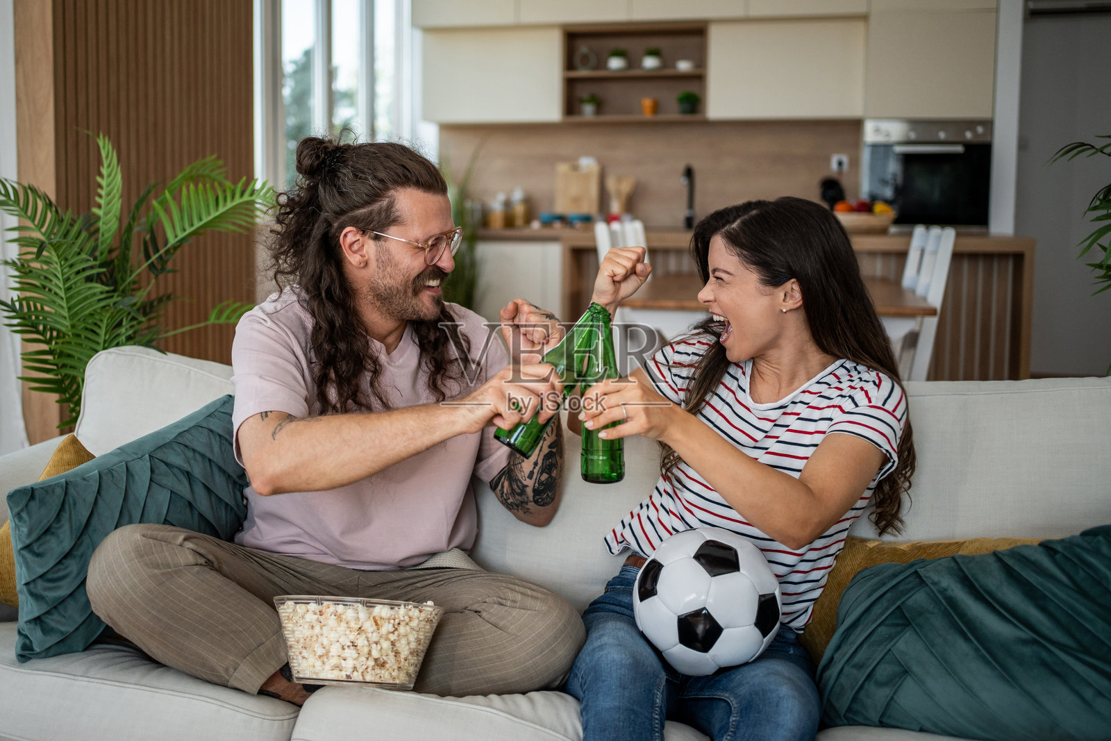 一对情侣在家观看足球比赛，举起啤酒瓶欢呼庆祝照片摄影图片