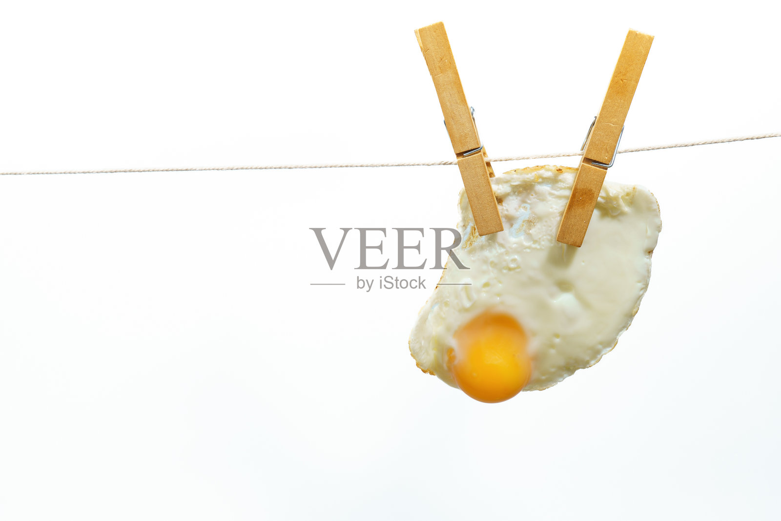 白色背景上晾衣绳上挂着的煎蛋和衣夹照片摄影图片