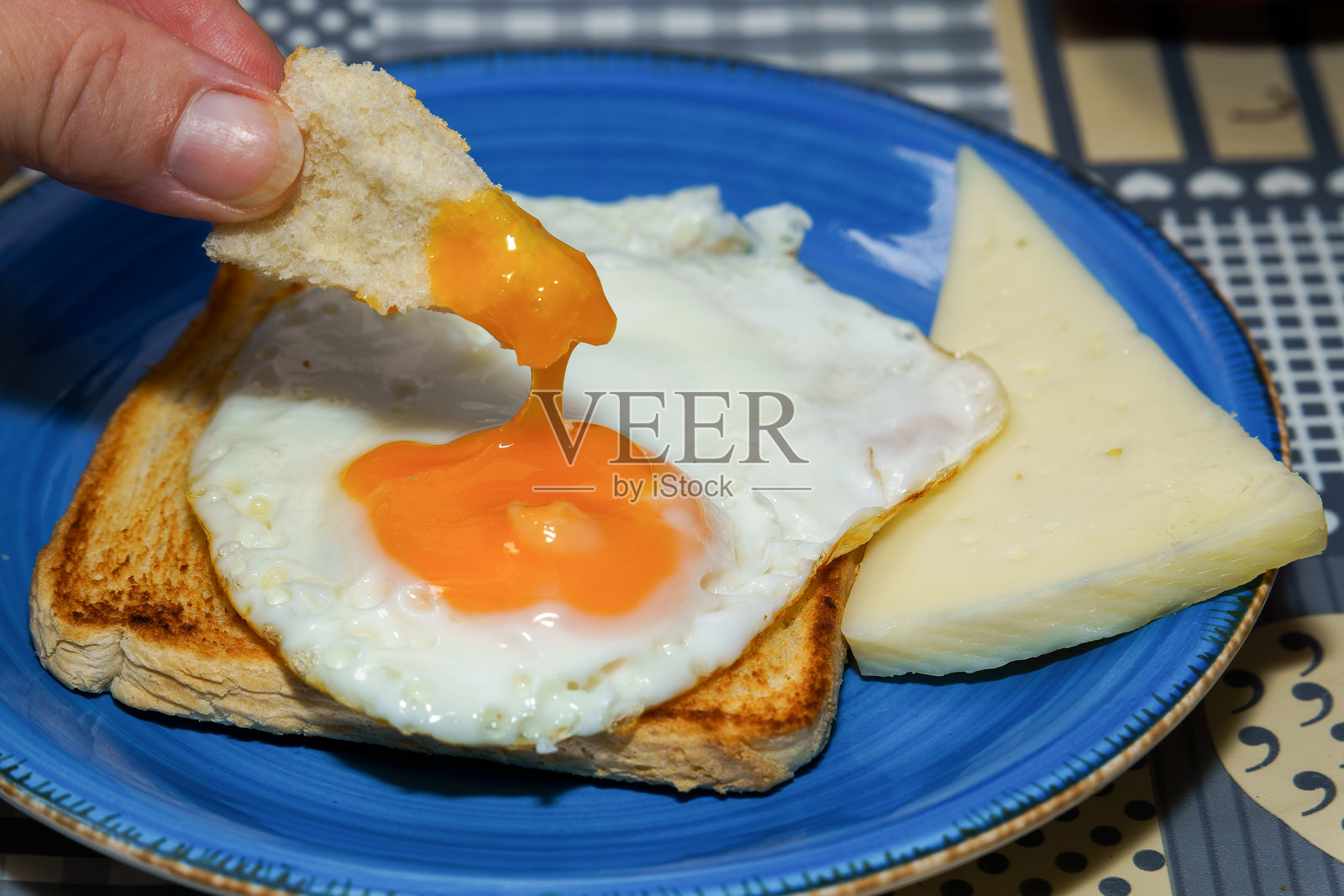 将吐司浸入流动的蛋黄中，旁边有奶酪，放在蓝色盘子上照片摄影图片