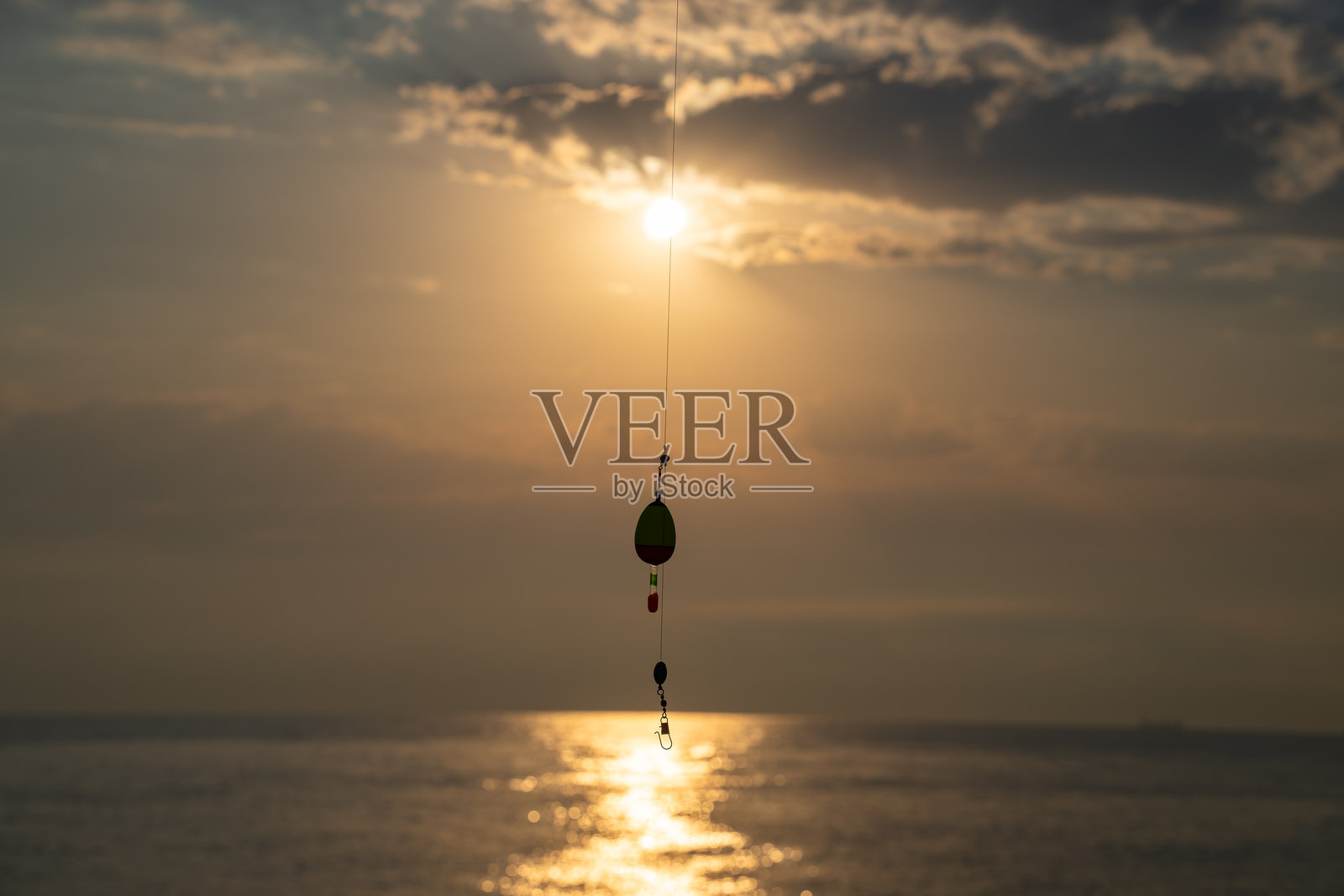 日落时分，海面上悬挂着钓鱼浮漂。钓鱼线在金色阳光下的剪影，浮漂轻轻摇晃。宁静的晨景。照片摄影图片