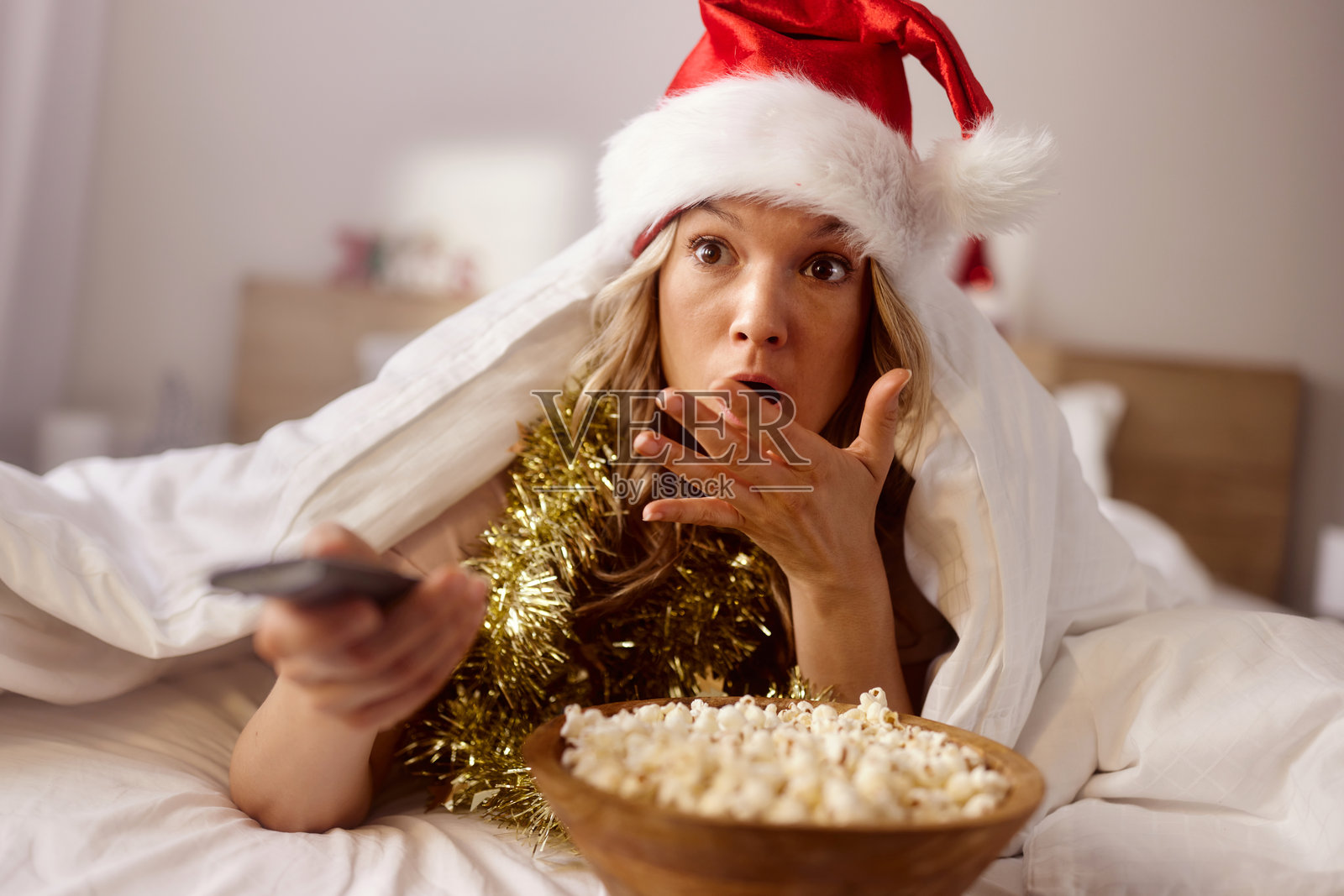 惊讶的女人在新年早晨躺在床上观看犯罪电影。照片摄影图片