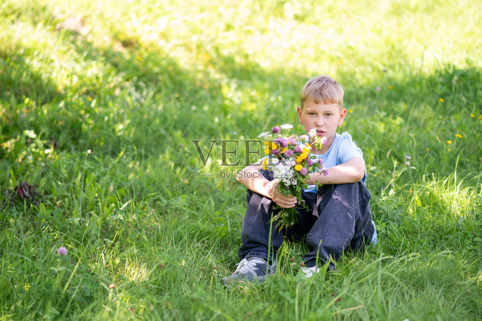 坐在草地上的少年手捧野花束照片摄影图片