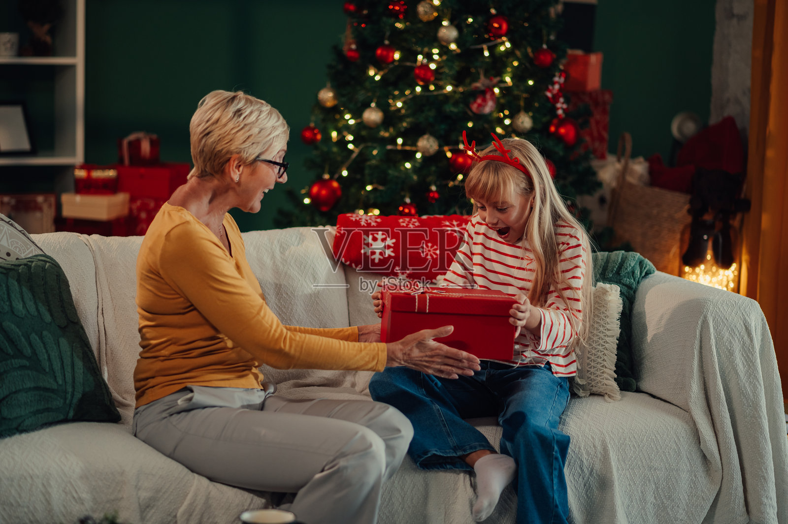 祖母在沙发上给兴奋的 granddaughter 送圣诞礼物照片摄影图片