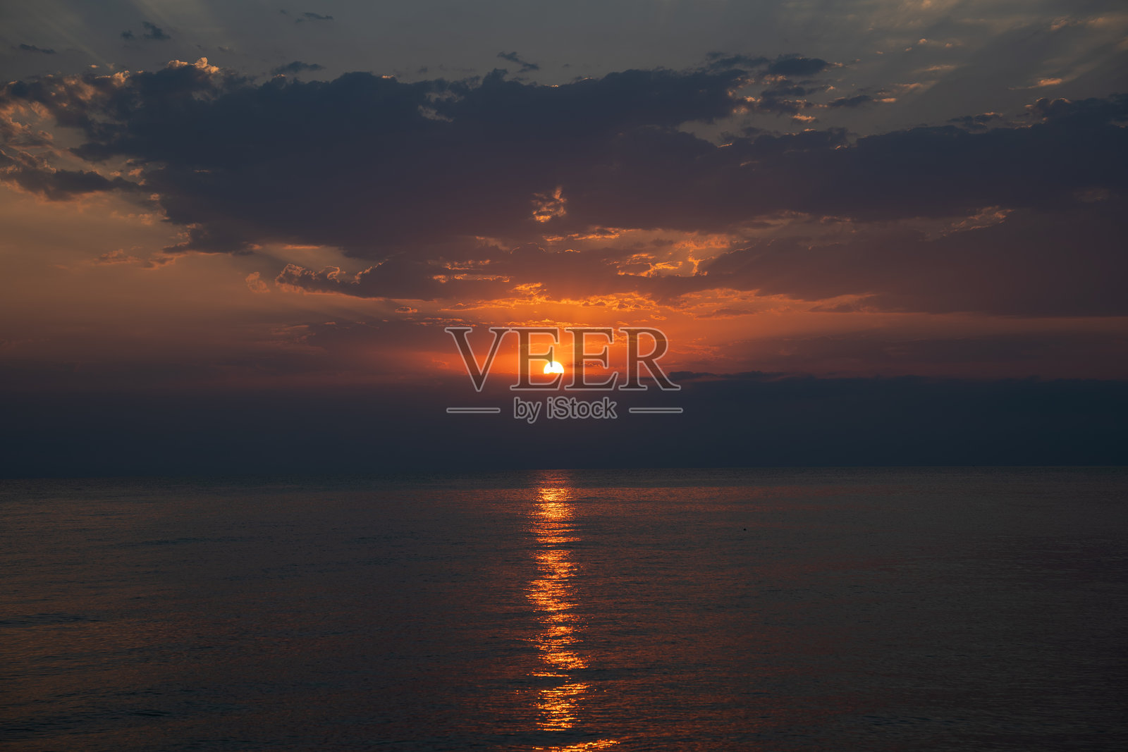 明亮的太阳在平静的海面上升起，创造出鲜艳的橙色和紫色天空，水面上闪烁着倒影。照片摄影图片