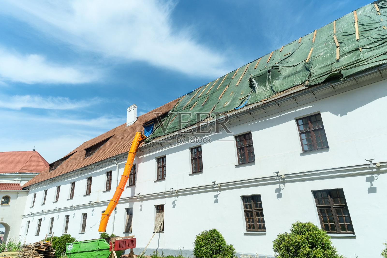 历史建筑需要仔细翻修，建筑废料通过一个橙色的滑道在屋顶维修期间运输。老建筑的翻修。屋顶正在施工中。照片摄影图片