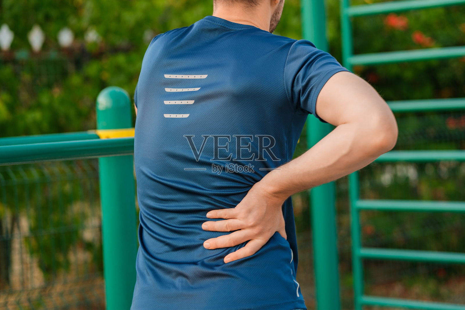 男子在公共公园锻炼后伸展身体，感受背部不适，天气炎热。照片摄影图片