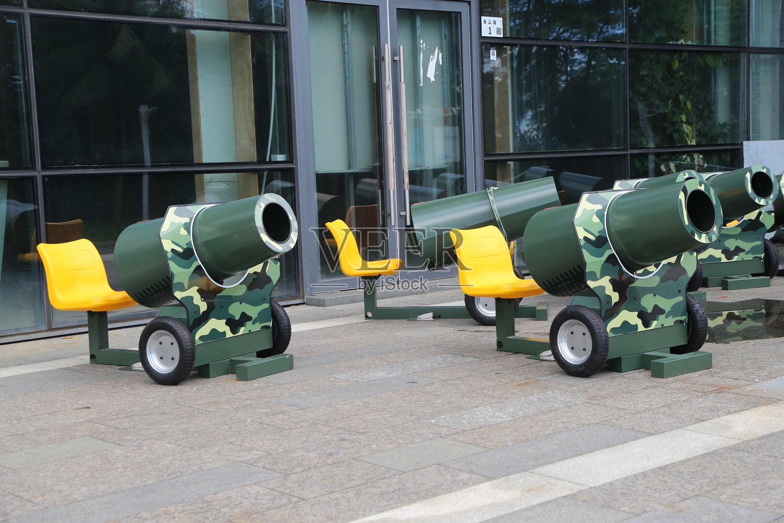 在建筑物前，有一个户外展示，展示着四辆涂有迷彩绿的混凝土搅拌车和带轮子的黄色座椅。照片摄影图片