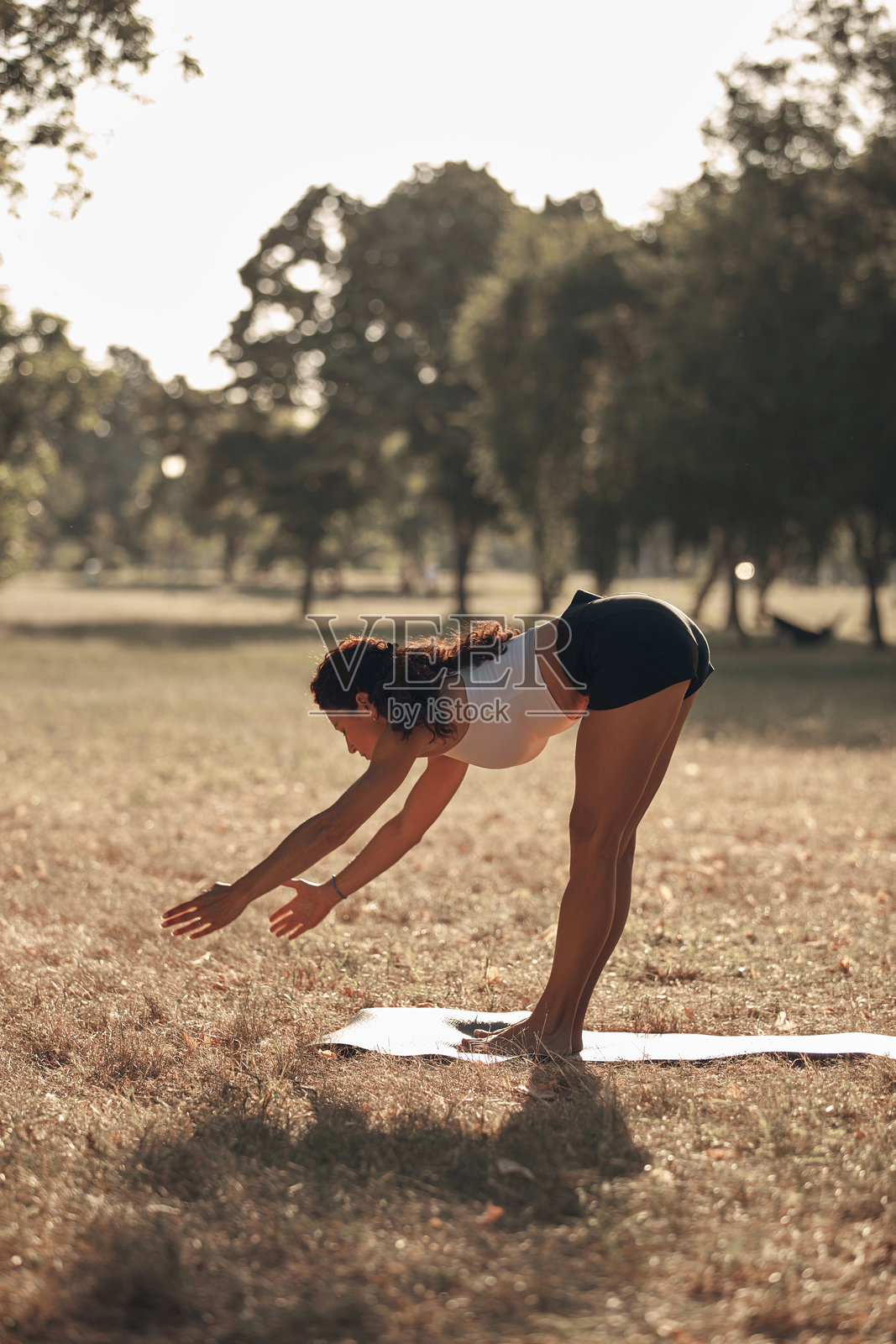 女人在炎热的夏日阳光下的公园里练习瑜伽和拉伸。照片摄影图片