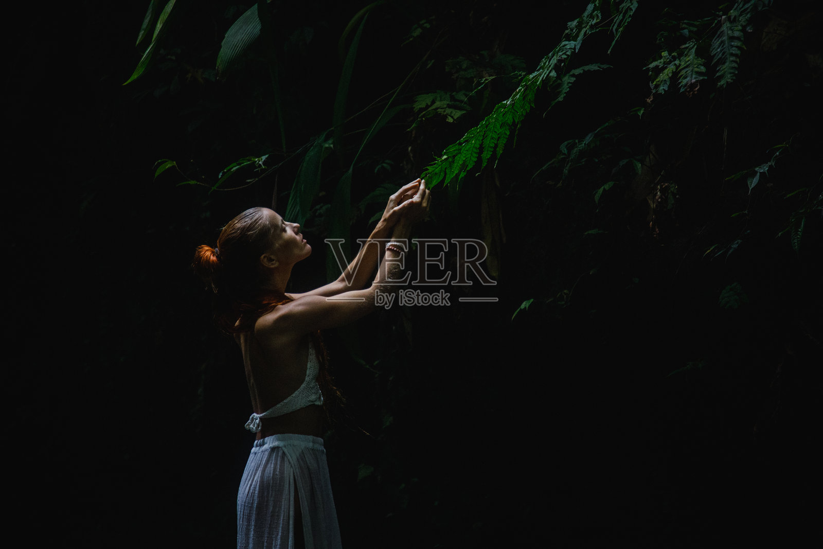 在热带森林中，一位女性欣赏着被郁郁葱葱的绿植环绕的叶子。照片摄影图片