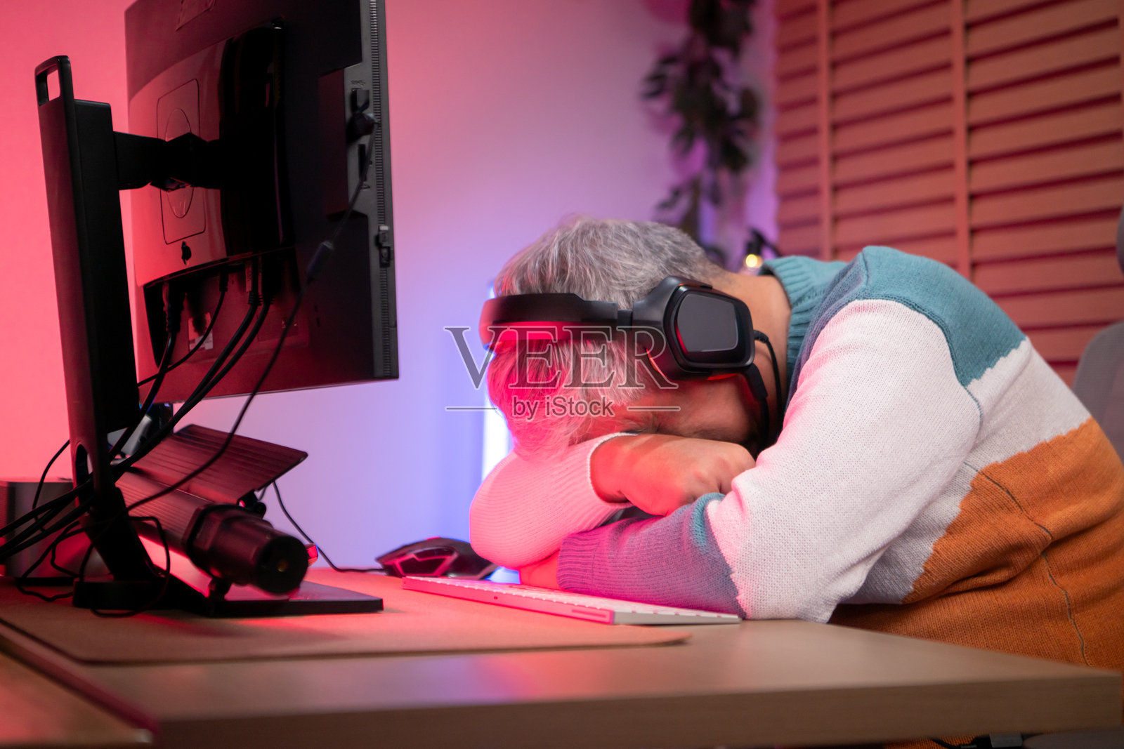 戴着耳机的老年男性玩家在色彩缤纷的游戏环境中使用台式电脑游戏照片摄影图片