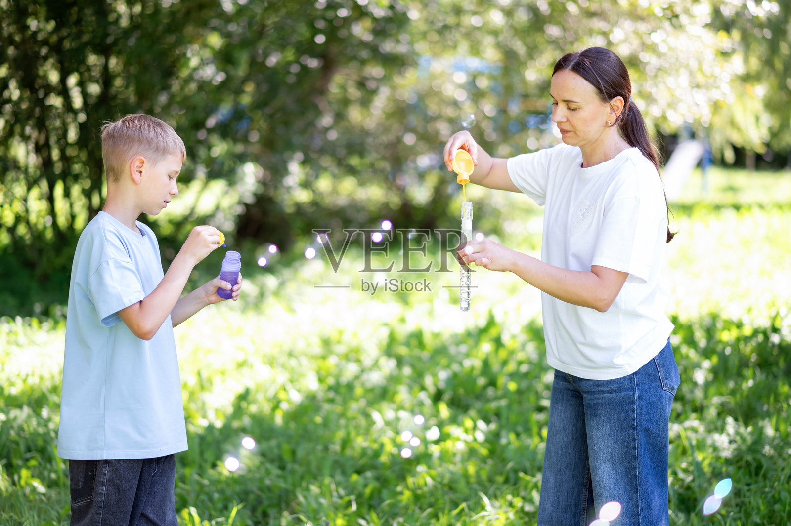 快乐的母亲和青少年儿子在夏季公园享受肥皂泡泡照片摄影图片