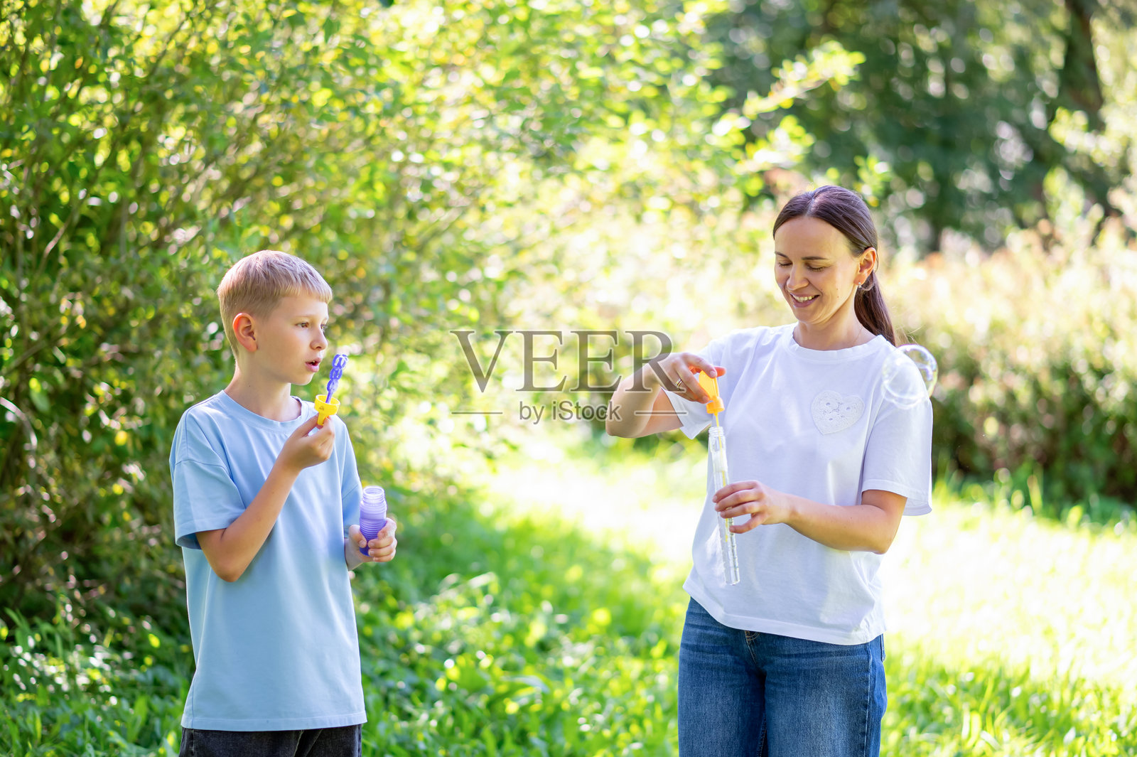 母亲和青少年男孩在夏季公园里快乐地吹泡泡照片摄影图片